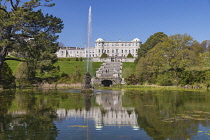 Ireland, County Wicklow, Enniskerry, Powerscourt Estate House and Gardens, Powerscourt House reflected in the Triton Lake with fountain shooting into the air.