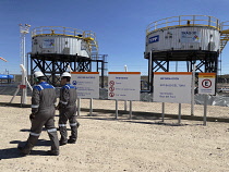 Argentina, Neuquen Province, Vaca Muerta, YPF personnel walk past oil and water storage tanks for onshore unconventional oil and gas production.