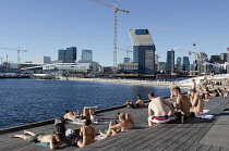 Norway, Enjoying the sun at Sørenga in front of Oslo ÂBar CodeÂcommercial district.