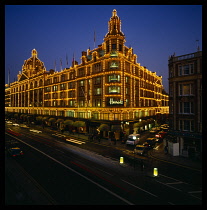 England, London, Harrods store exterior illuminated at night with light trails from passing traffic.