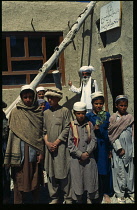 Afghanistan, Gardez, School teacher standing outside with group of schoolboys using bell made from a grenade.
