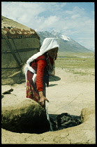 Afghanistan, General, Kirghiz nomad woman cooking in open topped clay oven outside yurt.