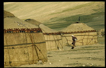 Afghanistan, General, Kirghiz  woman walking between yurts in bleak landscape.
