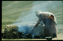 Afghanistan, General, Kirghiz woman cooking over open fire with surrounding wall of packed mud or clay.