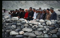 Afghanistan, General, Kirghiz men praying along stone wall of open air camp mosque.