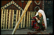 Afghanistan, General, Nomadic Kirghiz woman seated beside reed screen and hanging textiles inside traditional ger.