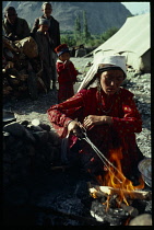Afghanistan, General, Kirghiz nomad woman cooking over open fire with children and older man standing behind her.