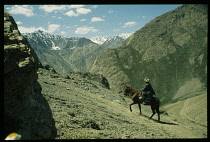 Afghanistan, Kirghiz, Man riding a horse up a hill overlooking a deep valley.
