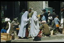 Afghanistan, Kabul, Street market with two women in burqas passing roadside male vegetable vendors.