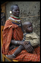 KENYA, Great Rift Valley, Kakuma, Turkana woman wearing mutiple beaded necklaces sitting with child at a campfor destitutes.