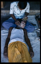 INDIA, Uttar Pradesh, Varanasi, Young boy being made up for Ramlila festival where the story of Lord Rama is enacted.  Gold leaf is placed on the face as part of decorative  floral pattern.