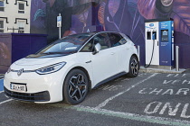 Ireland, County Wexford, New Ross, E-car being charged at an electric car charging point with a mural by Dutch artist Nina Valkhoff showing a Norman warrior woman and her horse behind.