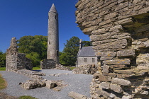 Ireland, County Laois, Timahoe Round Tower partly framed by a wall of a monastic ruin with a former Church of Ireland church which is now a heritage centre.