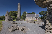 Ireland, County Laois, Timahoe Round Tower partly framed by a wall of a monastic ruin with a former Church of Ireland church which is now a heritage centre.