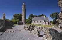 Ireland, County Laois, Timahoe Round Tower partly framed by a wall of a monastic ruin with a former Church of Ireland church which is now a heritage centre.