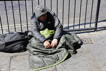 England, London, Trafalgar Square, Homeless man sat on pavement against metal railings.