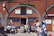 England, East Sussex, Brighton, Smokehouse fish sandwich vendor in arches by seafront promenade busy with summer tourists.