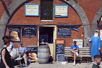 England, East Sussex, Brighton, Smokehouse fish sandwich vendor in arches by seafront promenade busy with summer tourists.
