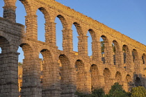 Spain, Castile and Leon, Segovia, Early morning golden light on the Aqueduct of Segovia, a Roman aqueduct with 167 arches built around the first century AD to channel water from springs in the mountai...