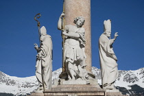 Austria, Tyrol, Innsbruck, Annasaule or St Anne's Column on Maria Theresien Strase dating from 1706, detail showing from left St Cassian, St George and St Vigilius with snow covered mountains in the b...