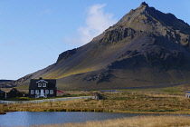 Iceland, Snaefellsnes Peninsula National Park, old fishing village of Hellnar with private house below volcanic mountain.