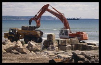 England, Dorset, Weymouth, Crane and truck on the beach transferring large stone blocks to build up the sea defences.