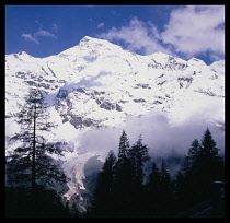 Austria, Tyrol, Grosslockner Peak, Snow covered mountain peak with smoke and trees in the foreground.