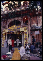 India, Rajasthan, Jaipur, Street vendors outside shop building decorated with flowers and hung with coloured lights.