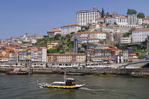 Portugal, Porto, Vila Nova de Gaia, Decorated tourist boat with passengers in transit and Rabelo cargo boats plus the Ribeira area of Porto in the background.